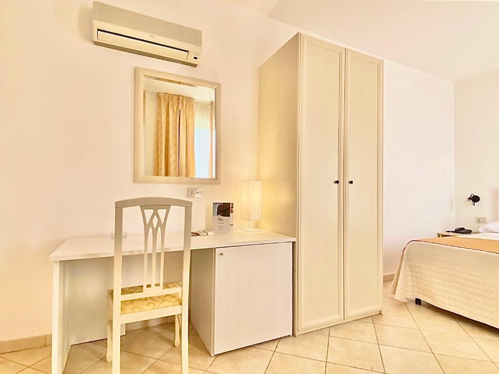 Gaiša viesnīcas numura daļa ar rakstāmgaldu, krēslu un skapi, kas nodrošina komfortu un praktiskumu. Pievienots spogulis un gaisma, radot mājīgu atmosfēru.