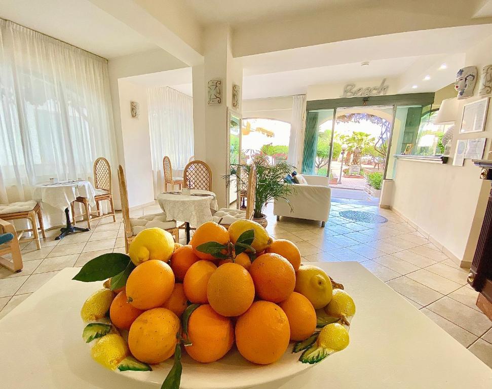 Svaigu augļu grozs ar apelsīniem un citroniem, novietots gaišā telpā ar ērtām mēbelēm un skatu uz dārzu. Telpa ir gaiša un viesmīlīga, radot patīkamu atmosfēru.