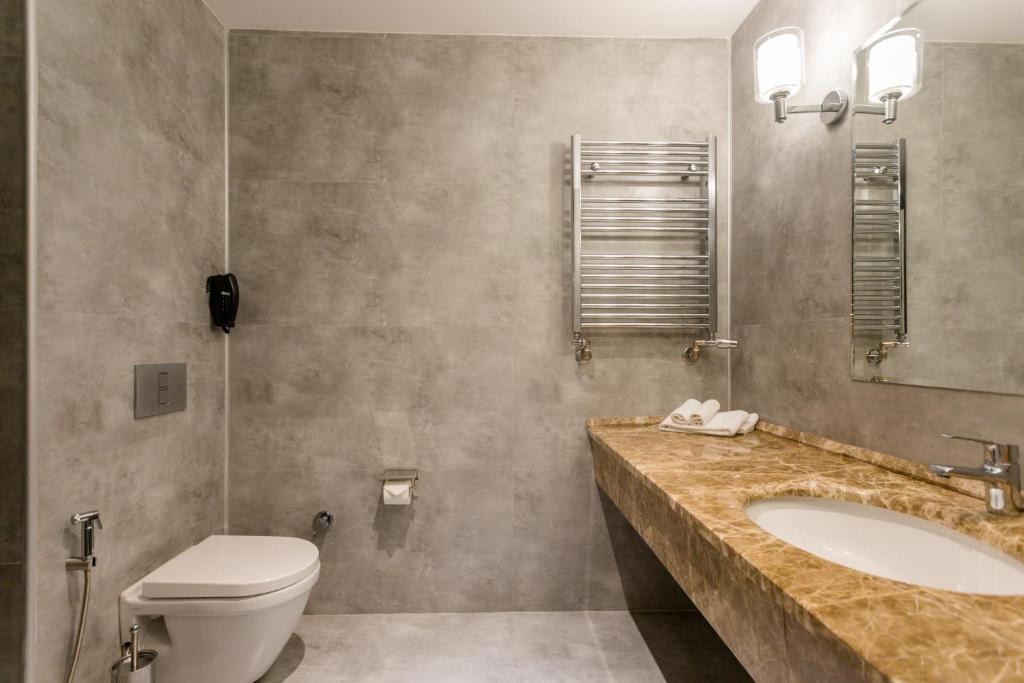 Mūsdienīgs vannas istabas interjers ar pelēkām flīzēm, marmora izlietni un hromētu radiatoru. Izgaismots ar divām sienas lampām un spoguli.