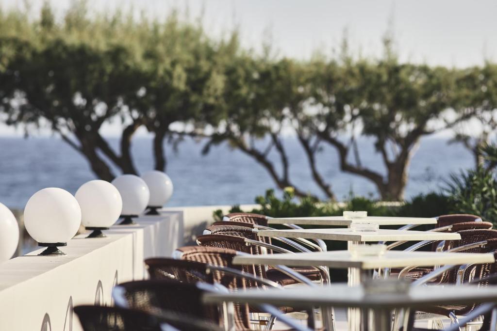 Terases galdi un krēsli ar baltiem apgaismojuma elementiem, izgaismota pie jūras, ar zaļiem kokiem fona.