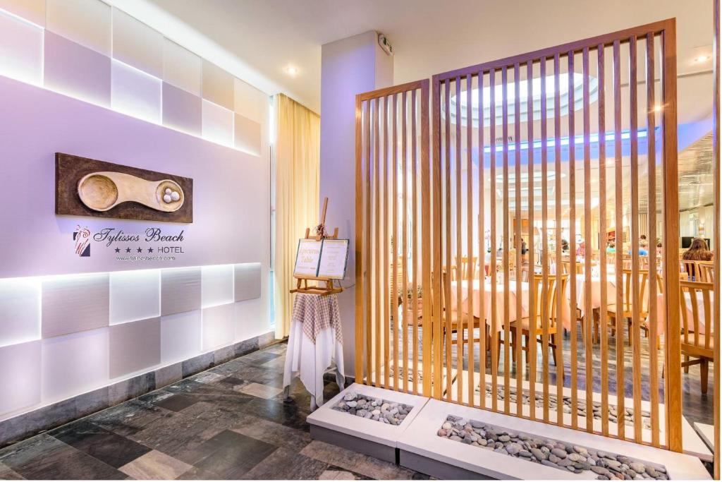 Mūsdienīga restorāna iekārtojuma skats ar koka žogu un elegantām detaļām, kas atrodas Tylissos Beach hotel. Restorāna atmosfēra ir gaiša un aicinoša, piedāvājot viesiem patīkamu maltīti.