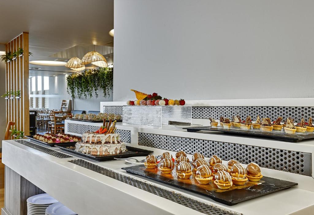 Kafejnīcas deserts stends ar dažādām kūkām un saldumiem, ieskaitot krāsainas mini kūkas un šokolādes delikateses, pievilcīgi izkārtots uz melnām platekrānām.