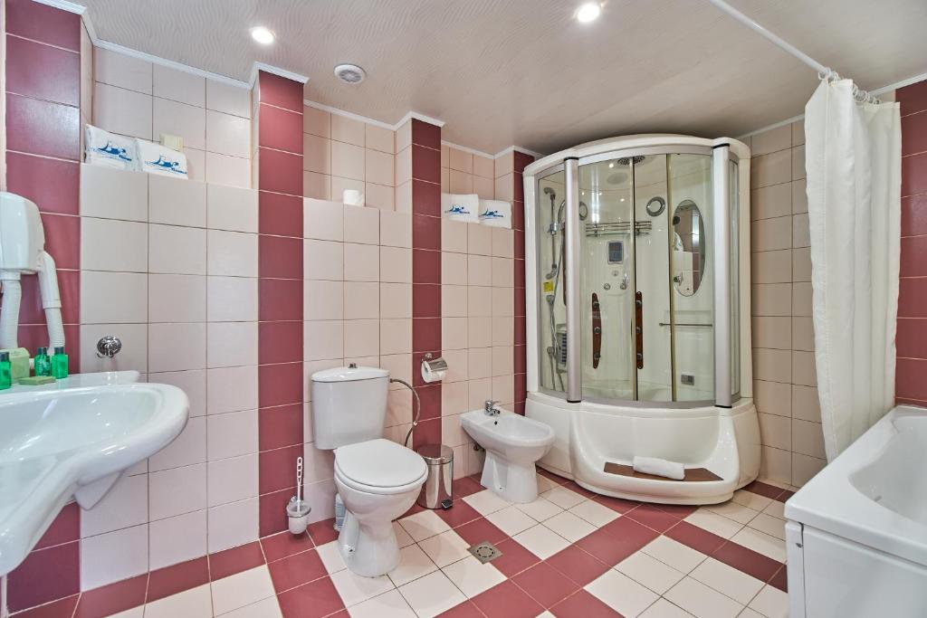 Mūsdienīgs vannas istabas interjers ar dušas kabīni, tualeti un izlietni, dekorēts ar rozā un baltām flīzēm. Vannas istabā ir pieejami higiēnas piederumi un aksesuāri.