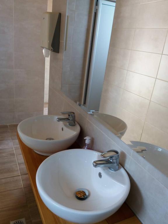 Divi moderni izlietnes trauki vannas istabā uz koka letes, ar spoguli un gaišu flīžu fona.