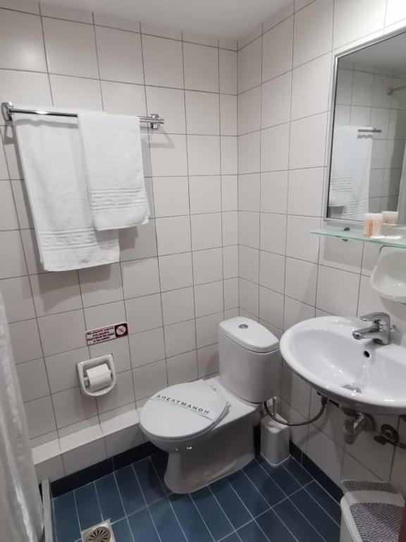Mazs un funkcionāls vannas istabas skats ar tualeti, izlietni un spoguli baltās flīzēs. Iekārtas ir moderns dizains un tīras.