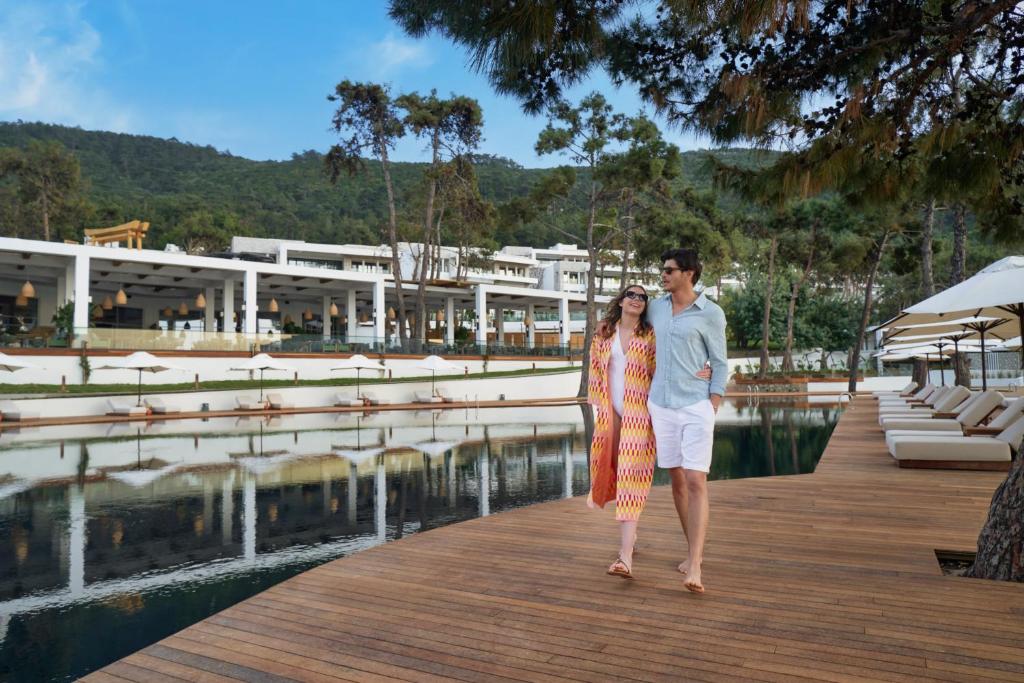Pāris staigā gar dīķi pie Rixos Premium Bodrum, baudot dabu.
