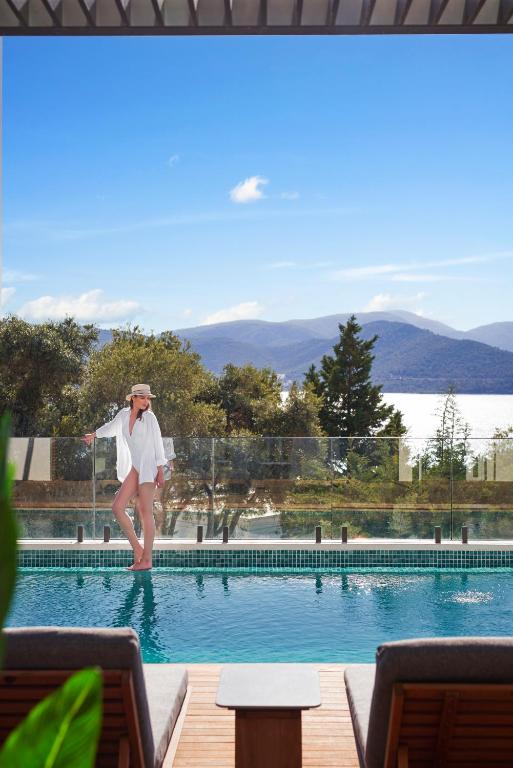 Sieviete stāv pie baseina Rixos Premium Bodrum, ar skatu uz jūru un kalniem.