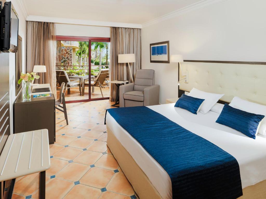 Mūsdienīgs viesnīcas numurs ar plašu logu, kas paver skatu uz terasi un dārzu. Numurā ir ērta gulta ar dekoratīvām spilveniem, krēsls un galds, radot patīkamu atmosfēru atpūtai.