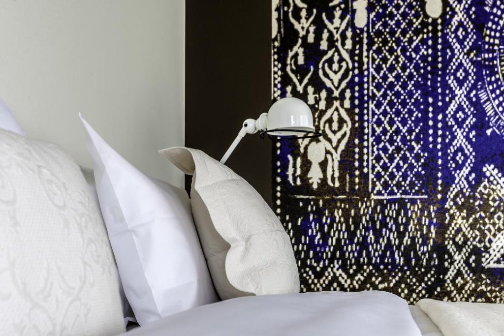 Mūsdienīga guļamistaba ar elegantu gultu, spilveniem un stilīgu lampu, fons rotāts ar zilu un baltu rakstu.