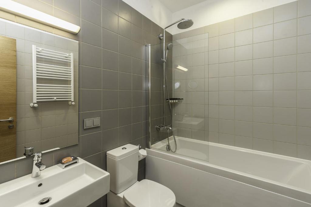Mūsdienīgs vannas istabas interjers ar pelēkām flīzēm, vannu un dušas kabīni. Tajā ir arī izlietne, tualete un siltuma radiators.