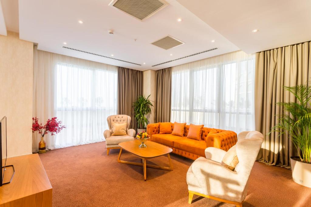 Mūsdienīga viesistaba ar gaišām aizkariem, oranžām dīvāna un krēslu akcentiem, kā arī dekoratīviem augiem, kas nodrošina siltu un viesmīlīgu atmosfēru.