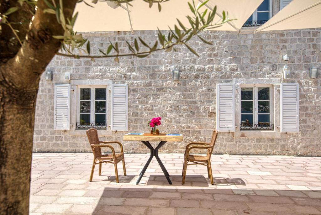 Elegants āra galds ar divām krēsliem, dekorēts ar ziediem, atrodas pie akmens sienas ar logiem un aizsargžalūzijām. Ideāla vieta relaksācijai un baudīšanai.