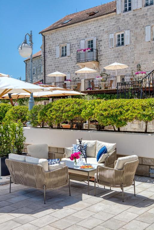 Moderns āra atpūtas stūris ar mīkstām mēbelēm, kas izvietotas zem saulessargiem, un skaistu ainavu ar augu dzīvžogu un akmens mājām fonā. Ideāla vieta relaksācijai un baudīšanai.