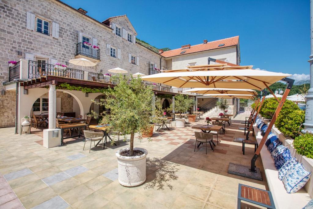 Skaista terase ar saulessargiem un augu kompozīcijām, kas izvietota starp akmens ēkām, radot mierīgu un patīkamu atmosfēru.