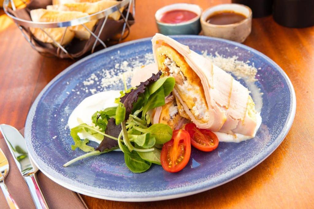 Garšīgs ēdiens uz zila šķīvja, ietverot tortilju ar pildījumu, svaigu salātu lapas un tomātus, pasniegts ar krējumu un mērci.