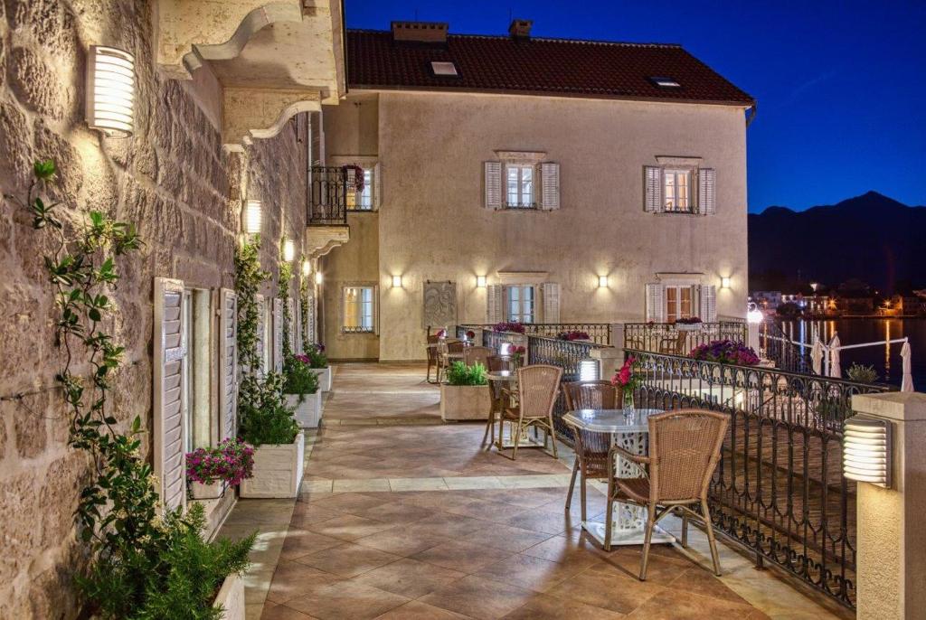 Elegantā terase ar galdiem un krēsliem, apzaļumota ar ziediem, piedāvā skaistu skatu uz ūdeni un kalniem, kad saule noriet. Gaismas radītais atmosfēras noskaņojums pievērš uzmanību nakts ainavai.