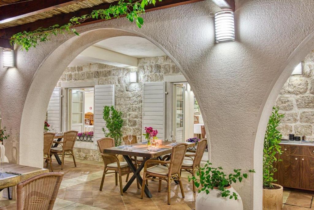 Eleganta restorāna iekārtojums ar arku un galdiem, kas apstādīti ar zaļumiem un ziediem. Gaisma un akmens sienas rada mājīgu atmosfēru.