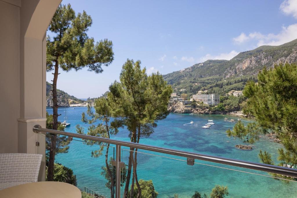 Skats no balkona uz skaistu jūras līci, ko ieskauj kalni un zaļi koki, radot mierīgu un idillisku atmosfēru. Ideāls galamērķis atpūtai.
