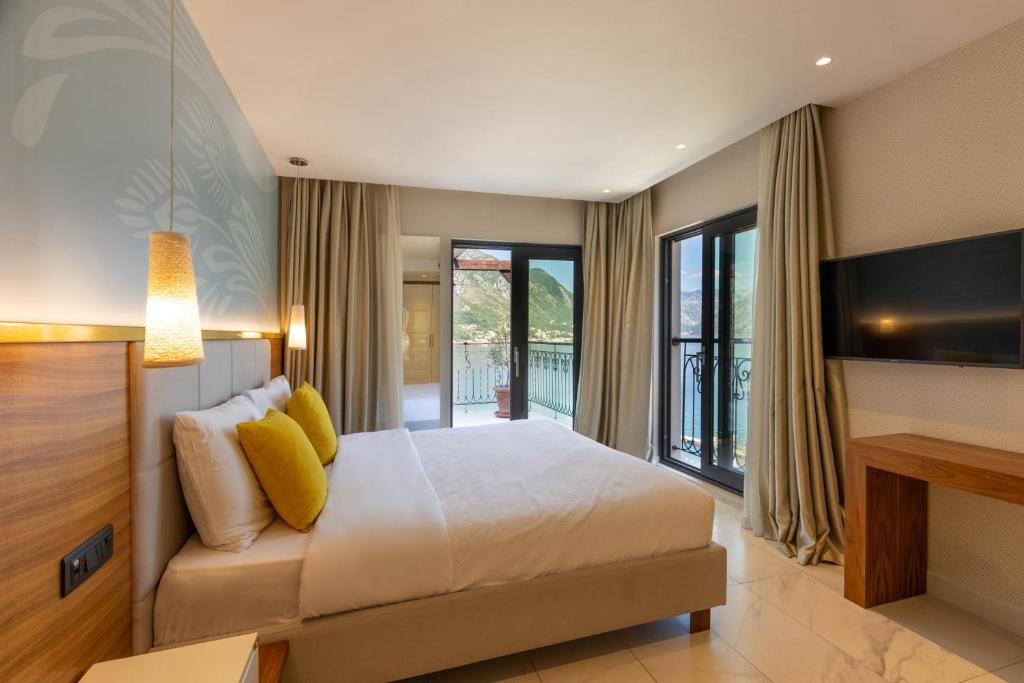 Mūsdienīgs guļamistabas interjers ar gultu, dīvānu un plašiem logiem, kas piedāvā skatu uz kalniem un ezeru. Telpu papildina gaismas elementi un neitrālas krāsas, radot relaksējošu atmosfēru.