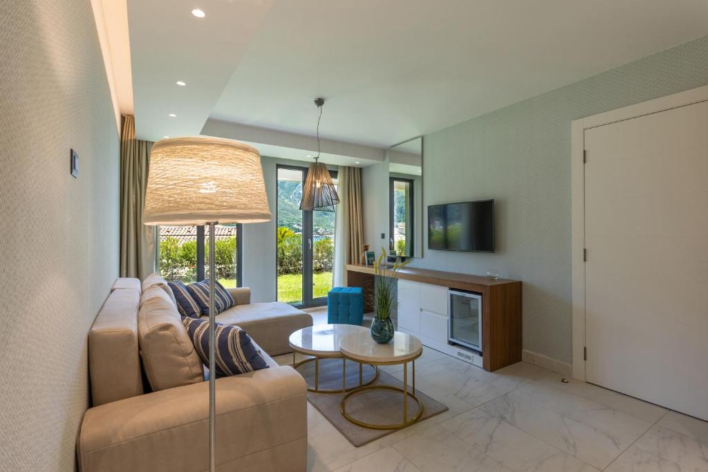 Mūsdienīgs viesistabas interjers ar dīvānu, apgaismojuma lampu un televizoru. Lielas loga durvis sniedz skatu uz dārzu un nodrošina dabīgu apgaismojumu.