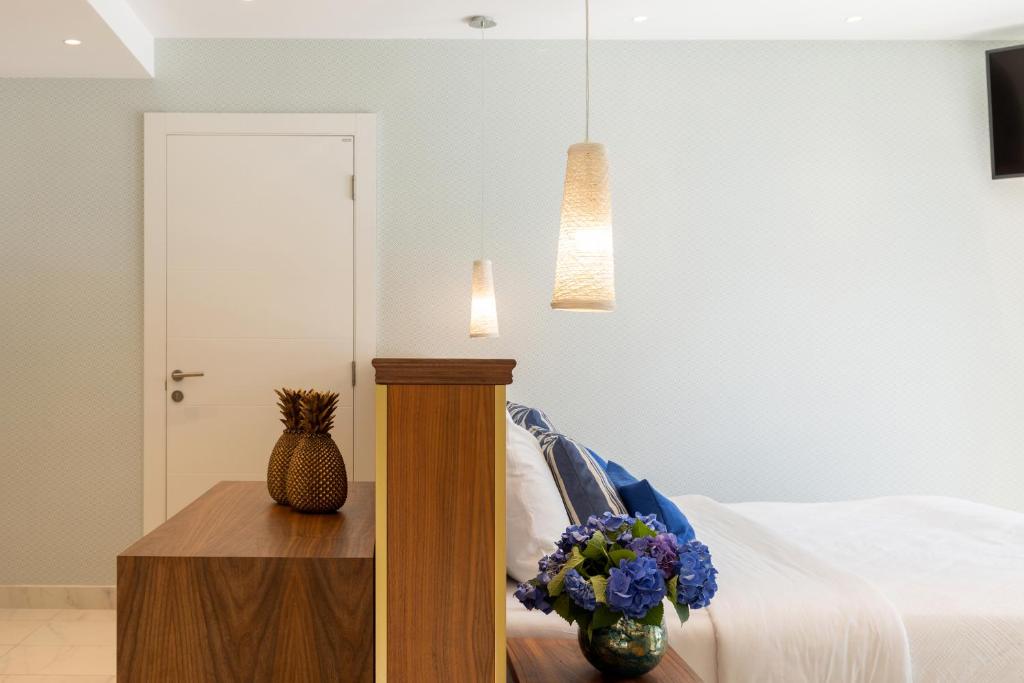 Mūsdienīgs guļamistabas interjers ar koka mēbelēm, zilu dekora elementu un ziedu kompozīciju. Gaismas avoti piešķir telpai siltu atmosfēru.