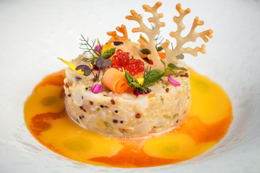 Skaisti noformēts ēdiens ar zivs salātiem, dekorēts ar dārzeņu un ziedu rotājumiem, kā arī garšaugiem. Apakšā ir krāsains mērces slānis.