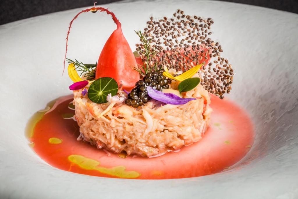 Gatavots gourmet ēdiens ar krabju gaļu, dekorēts ar ziediem, kaviāru un krāsainu mērcīti. Elegants un radošs pasniegšanas veids, kas uzsver kulinārijas mākslu.