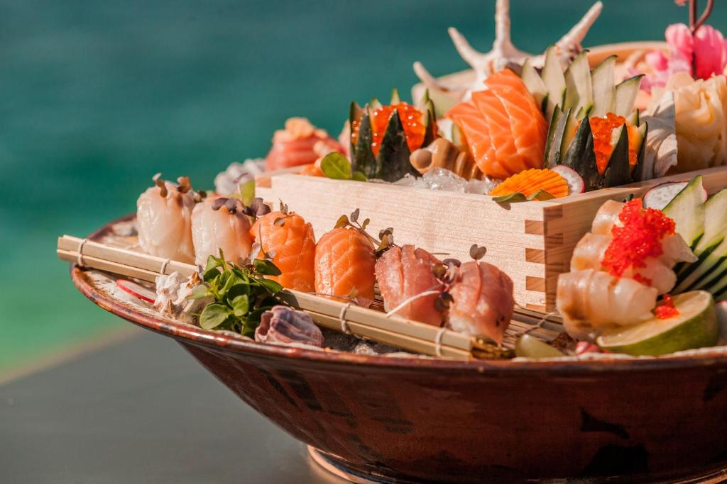 Svaiga suši šķīvis ar dažādiem jūras produktiem, dārzeņiem un dekoratīviem elementiem, pasniegts uz eleganta trauka.