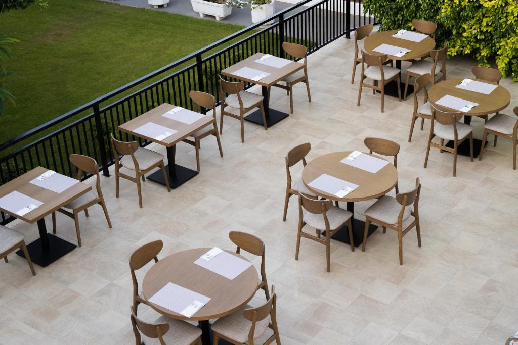 Terases restorāna zona ar apaļiem galdiem un koka krēslām, apstādījumi fonā. Ideāla vieta relaksācijai un ēšanai brīvā dabā.