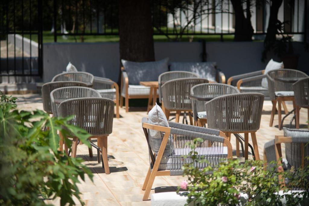 Dizainēti dārza krēsli ar pelēkiem spilveniem, novietoti uz koka grīdas, veido relaksējošu atmose vietu. Apkārt ir zaļumi un ziedošas rozes.