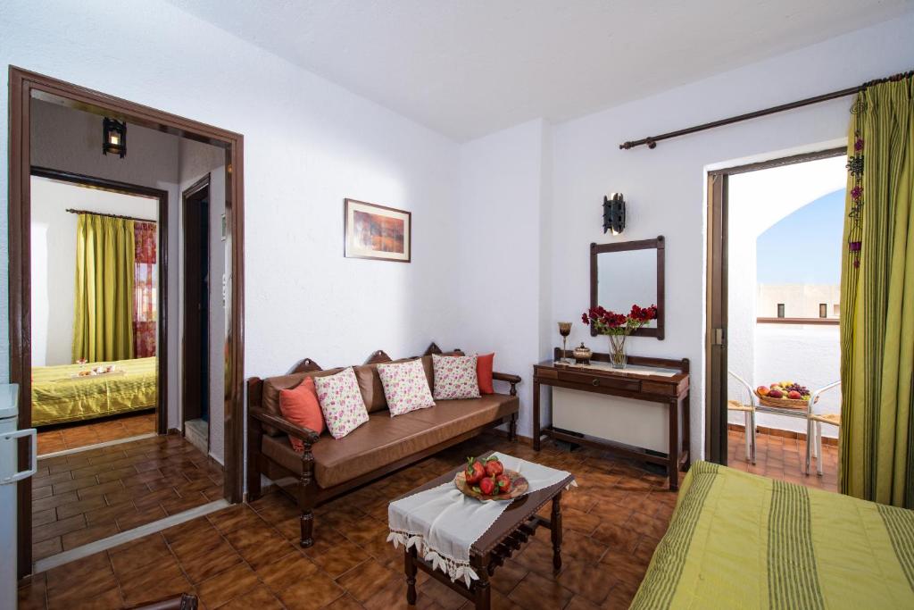 Labi iekārtota viesnīcas istaba ar dīvānu, spoguli un piekļuvi balkonam. Logā redzams zaļš aizkaru audums un guļamistaba ar dzeltenu gultu.