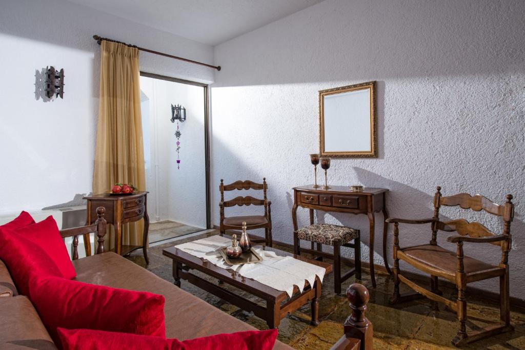 Gaiša dzīvojamā istaba ar sarkaniem spilveniem, koka mēbelēm un dīvānu, kas rada mājīgu atmosfēru. Logā ieplūst dabiska gaisma, uz galda atrodas dekoratīvas detaļas.