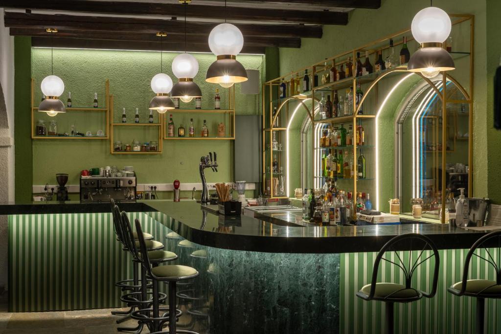 Mūsdienīgs bārs ar zaļām sienām, stilīgu apgaismojumu un dažādām alkoholiskajām dzērienu pudelēm. Bāra letes dizains ir elegants ar melnu virsmu un svītrainu apakšu.