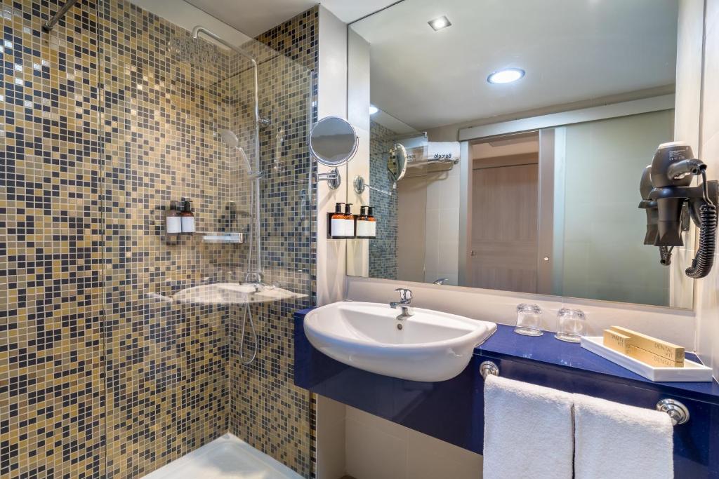 Moderns vannas istabas interjers ar mozaīkas flīzēm, dušu un izsmalcinātu izlietni. Vannas istabā atrodas arī higiēnas piederumi un spogulis.