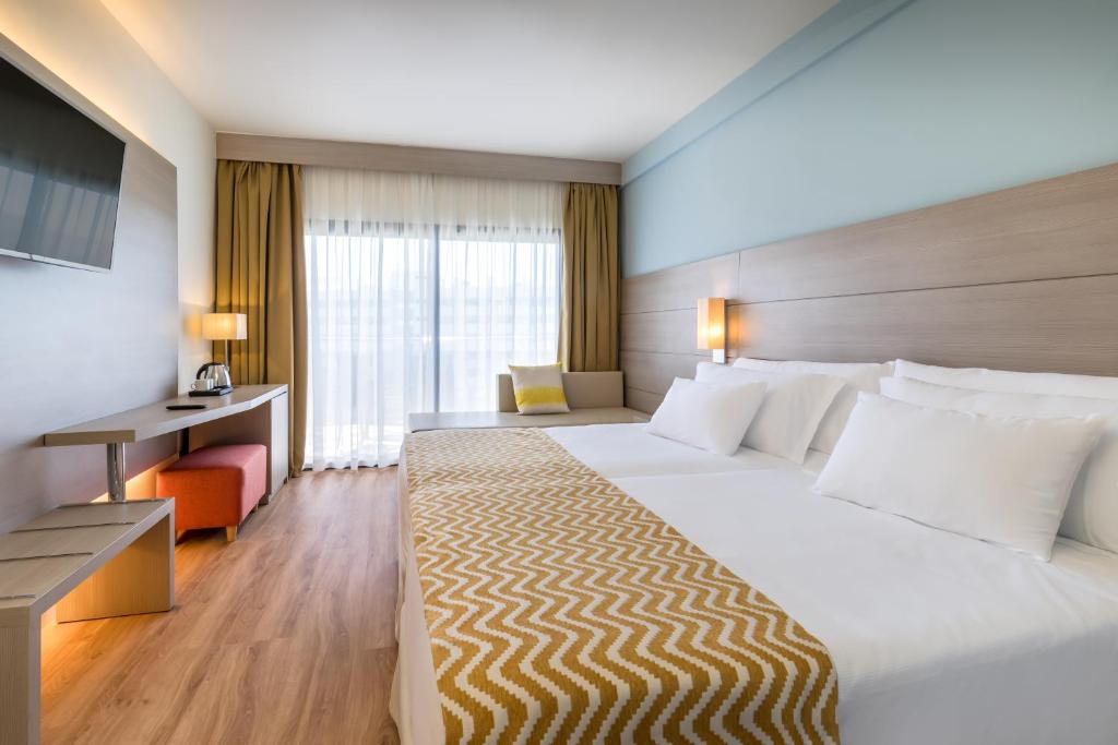 Mūsdienīga viesnīcas numura iekārtojums ar divām gultām, koka grīdu un lieliem logiem, kas ļauj ienākt dabiskajai gaismai. Numurā ir televizors, galdiņš un dīvāns, radot ērtu un relaksējošu atmosfēru.