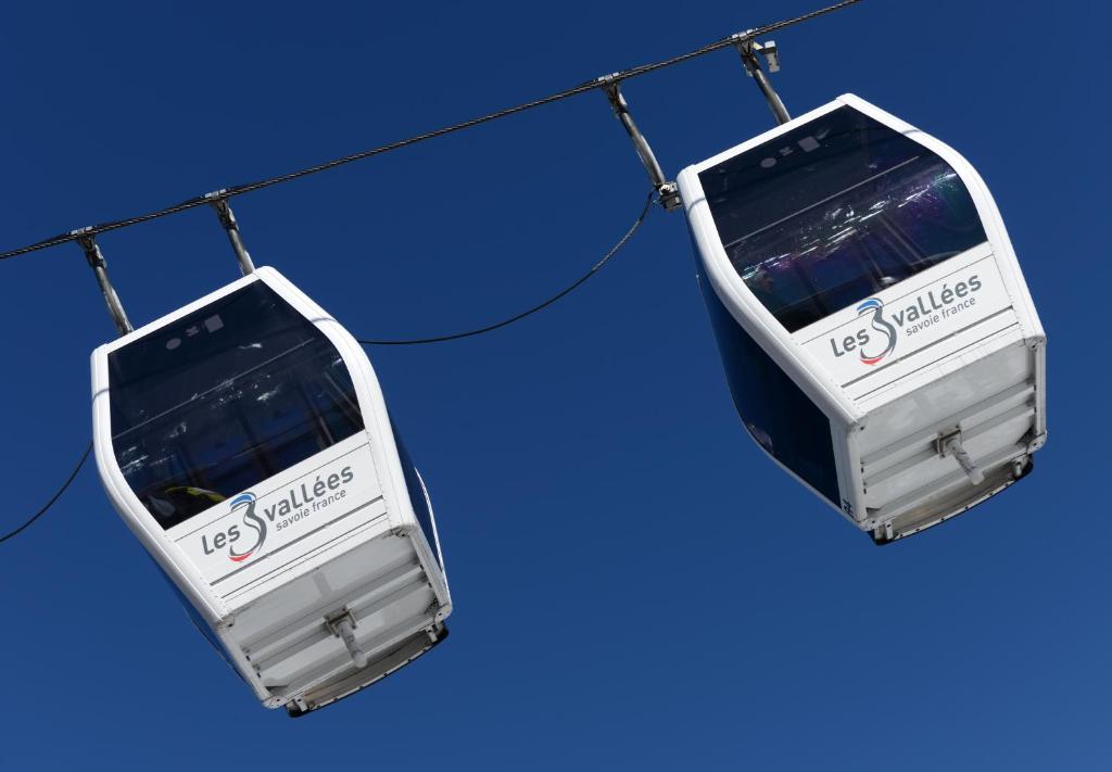 Gaisa tramvajs ar logotipu "Les 3 Vallées" izceļas pret skaidru zilo debesi.