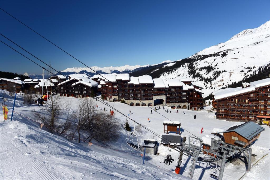 Sniegotā kalnu ainava ar slēpošanas kūrortu un pacelšanas iekārtām. Apmeklētāji baudījuši ziemas sportus, kamēr fona redzami sniegoti kalni.