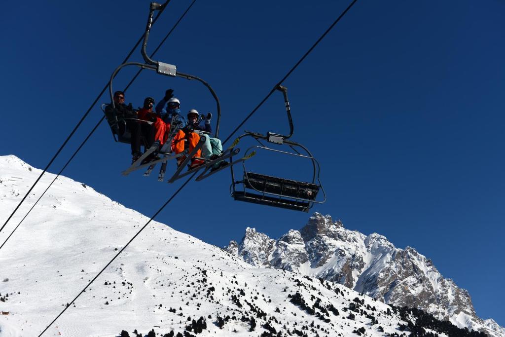 Slēpotāji izbaudījuši kalnu ainavas, braucot pa pacēlāju uz sniegotiem virsotnēm. Skaidrs zils debesis un majestātiski kalni veido ideālu ziemas atpūtas ainu.