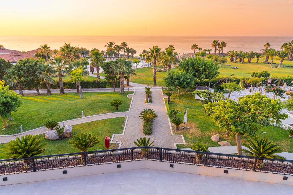 Saulrieta ainava ar zaļām palmu alejām un gleznainu pludmali, kas paveras no viesnīcas terases. Dārza ceļi un augu kompozīcijas piešķir mierīgu atmosfēru.