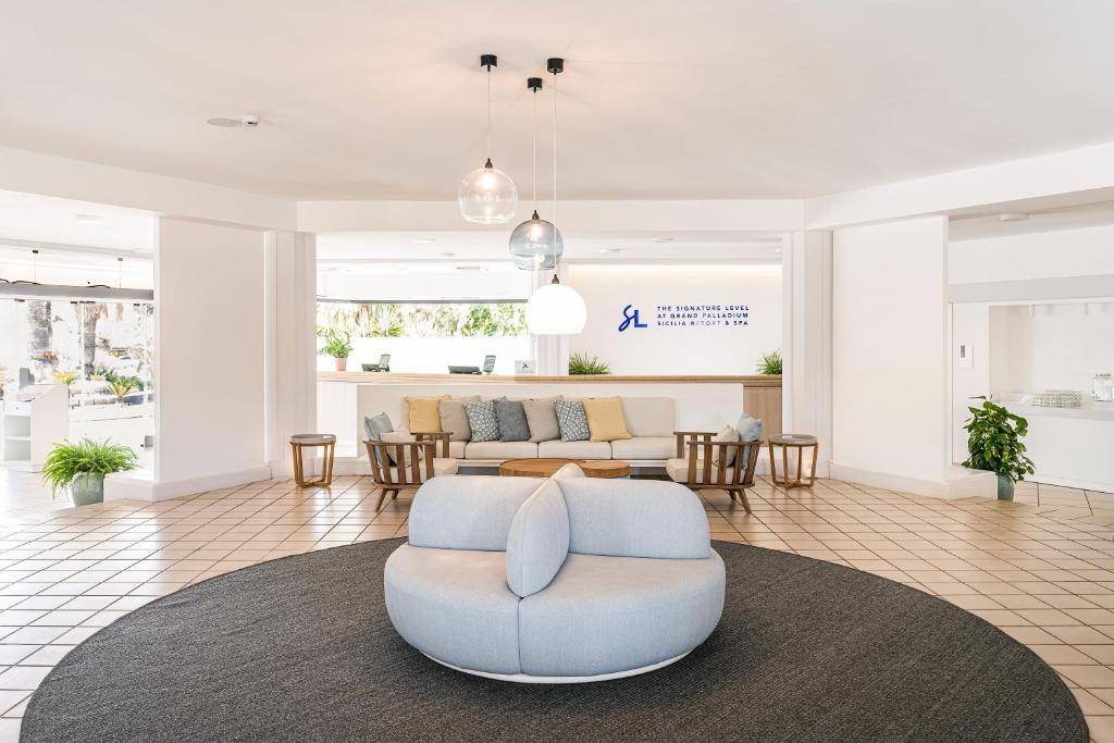 Mūsdienīgs viesnīcas reģistratūras interjers ar ērtām mēbelēm, gaišām krāsām un augiem, kas rada viesmīlīgu atmosfēru.