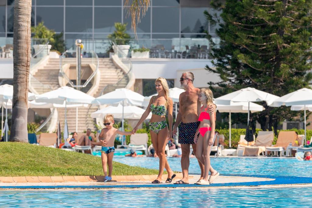Ģimene pie Miracle Resort Hotel baseina, saulainā dienā.
