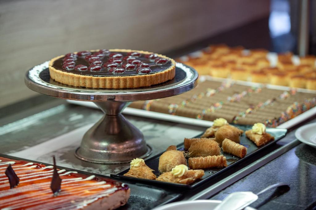 Deserts ar dažādiem kārumiem, tostarp ķiršu kūka, saldās vafeles un riekstu cepumi, kas izkārtoti uz melnas un sudraba šķīvja.