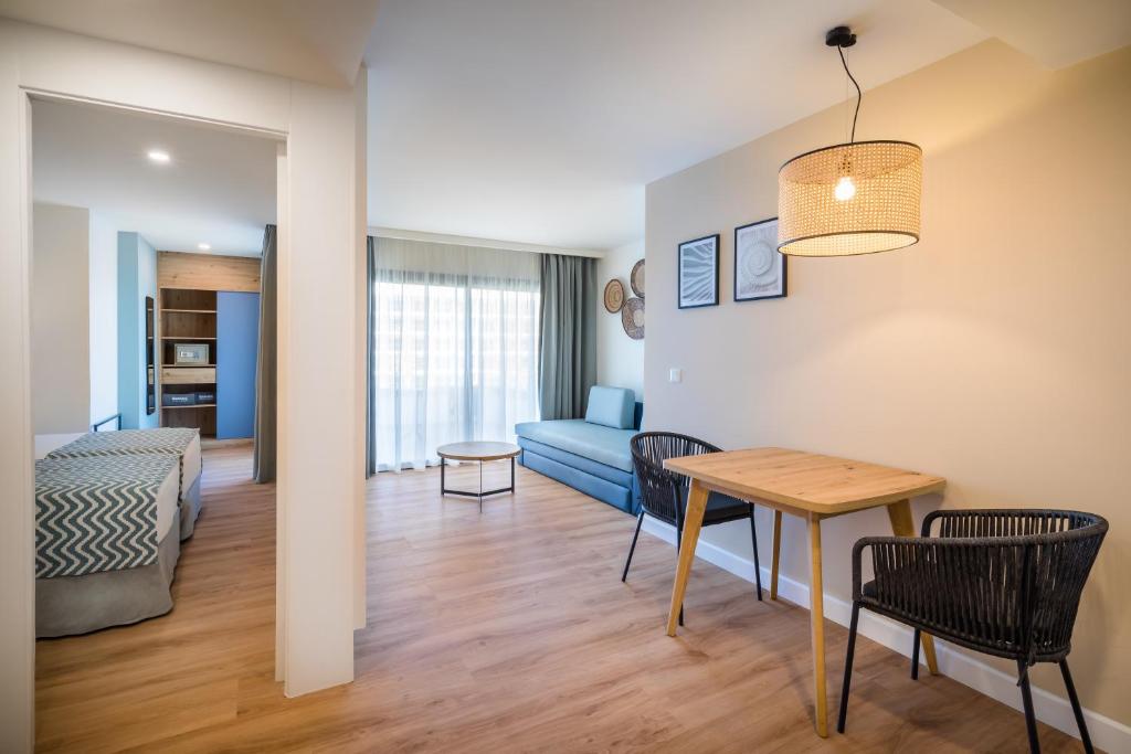 Mūsdienīgs viesnīcas numurs ar plašu dzīvojamo telpu, ērtu dīvānu, galds ar krēsliem un lieliem logiem, caur kuriem ieplūst dabisks apgaismojums.