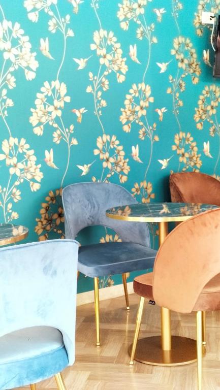 Stilīgs kafijas veikals ar ziedu rakstiem uz sienas un krāsainām krēsliem, radot patīkamu atmosfēru. Interjers ir moderns un uzaicinošs.