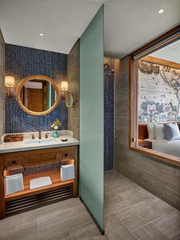 Mūsdienīgs vannas istabas interjers ar elegantu spoguli, koka izstrādājumiem un stilīgu flīžu apdari. Gaismas un krāsas harmonija rada relaksējošu atmosfēru.