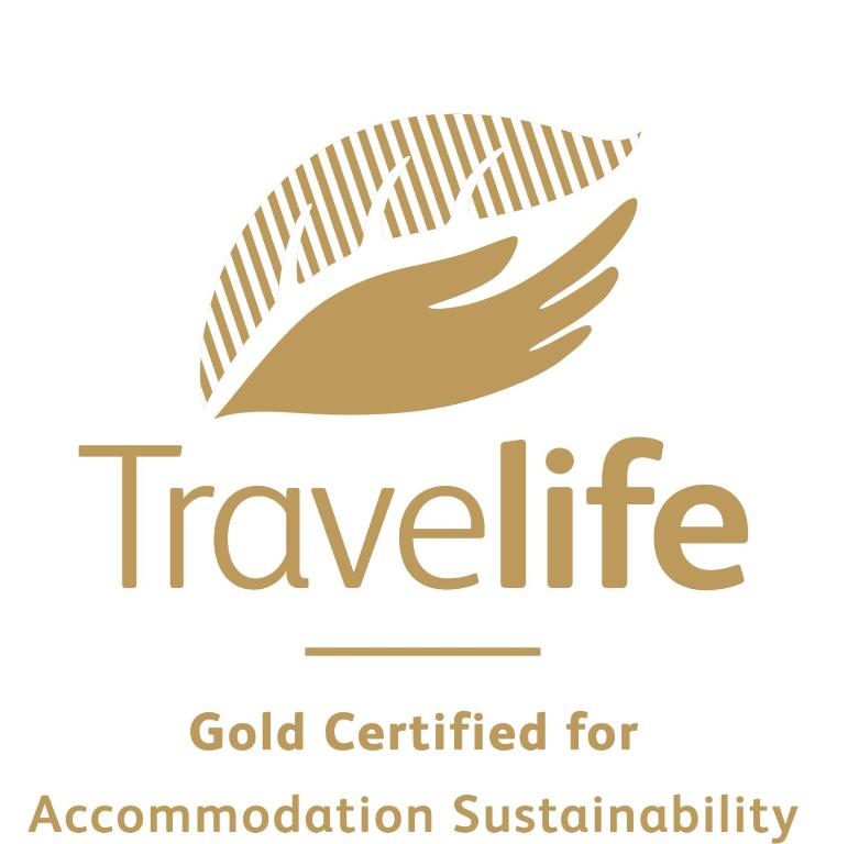 Travelife zelta sertifikāts ilgtspējīgas naktsmītnes nodrošināšanai, attēlota stilizēta roka un lapas simbolika.