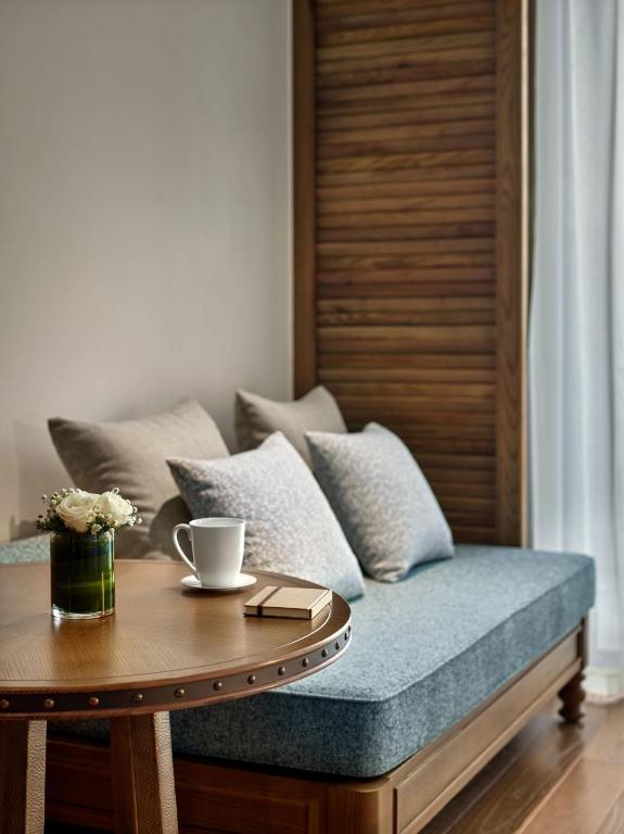 Mūsdienīga un mājīga viesistaba ar dīvānu, spilveniem un koka galdu, uz kura atrodas tase un ziedu pušķis. Ideāla vieta relaksācijai un atpūtai.