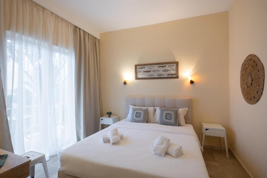 Mūsdienīgs guļamistabas interjers ar plašām logu aizkariem, gultu ar dekoratīvajām spilveniem un minimālistisku dizainu. Telpā ir arī koka galdiņš un dekoratīvi elementi, kas piešķir mājīgu atmosfēru.