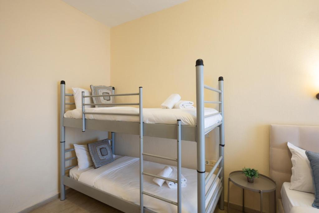 Divstāvu gulta ar spilveniem un dvieļiem, izvietota gaišā telpā ar neitrālām sienām. Telpā ir arī neliels galdiņš un dīvāns.