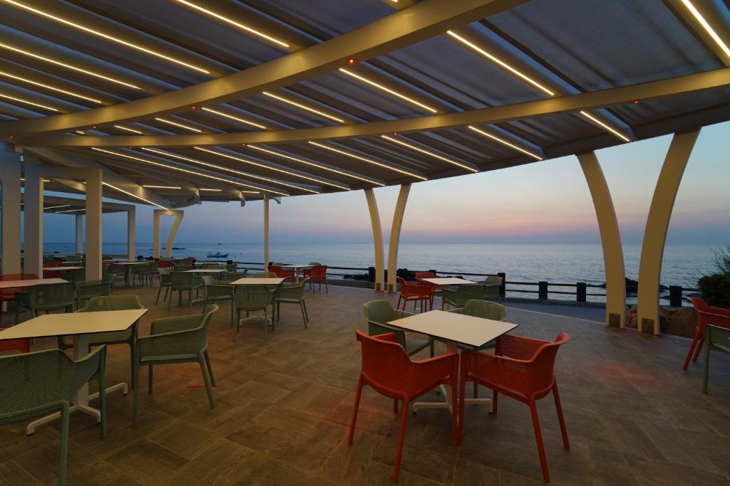 Moderns terases dizains pie jūras ar krāsainām mēbelēm un apgaismojumu, radot relaksējošu atmosfēru saulrietā.